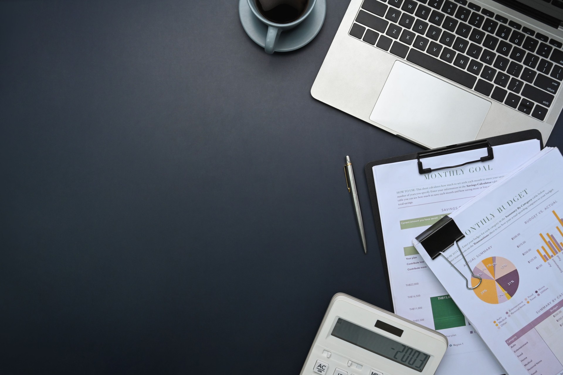 Top view of office desk with laptop, calculator, financial reports, and coffee cup on desk